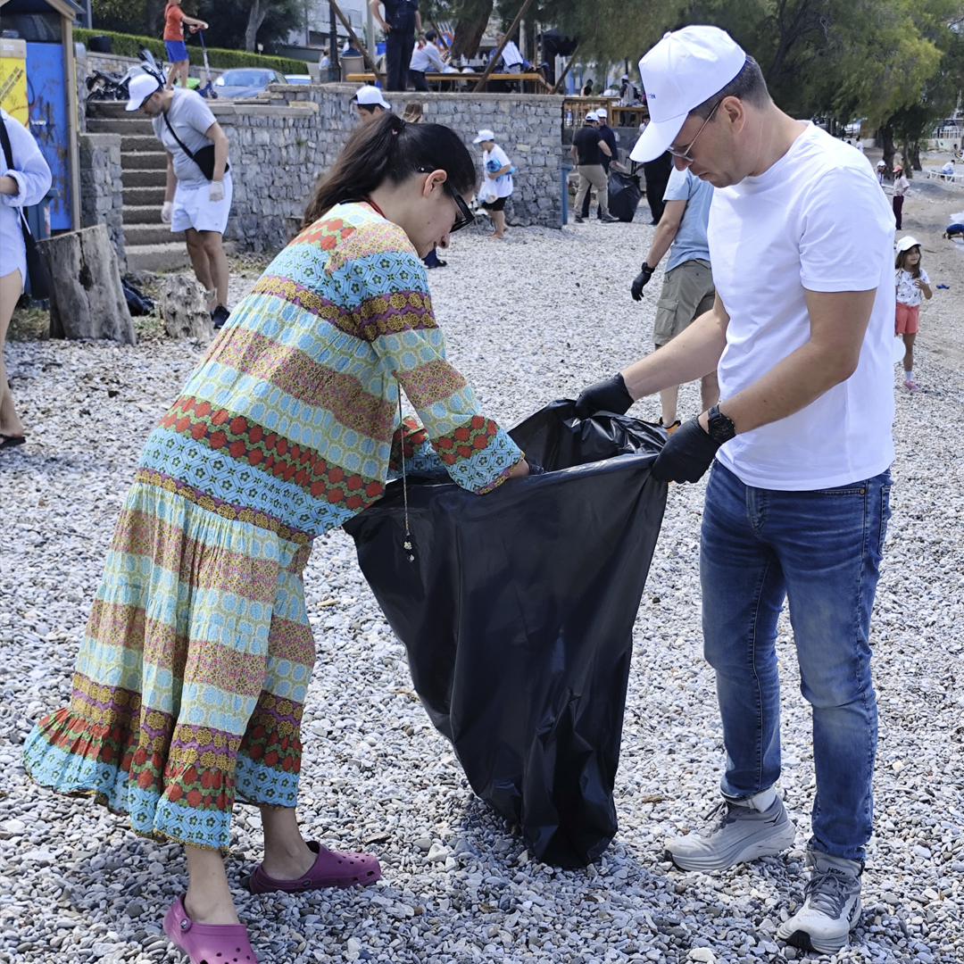 Δύο άνθρωποι της εταιρείας κρατούν μια σακούλα σκουπιδιών όπου μαζεύουν απορρίμματα από την παραλία.